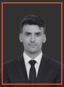Professional headshot of a man in a suit and tie against a dark gray background, facing the camera.