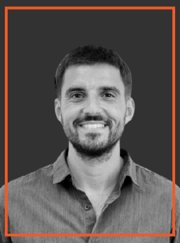Professional head-and-shoulders portrait of a smiling man with short dark hair and a trimmed beard, wearing a button-down shirt.