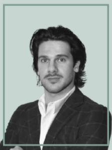 Portrait of a man with dark hair and light beard, wearing a white shirt and dark blazer, facing the camera.