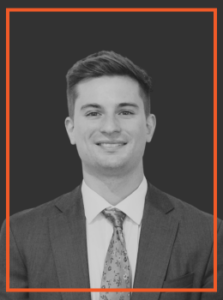 Professional headshot: smiling man in a suit and tie against a dark background.