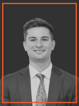 Professional headshot: smiling man in a suit and tie against a dark background.