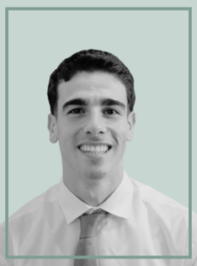 Head-and-shoulders portrait of a smiling man in a white shirt and tie against a pale green backdrop.