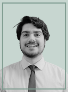 Head-and-shoulders portrait of a smiling man in a white shirt and tie, against a light teal background.